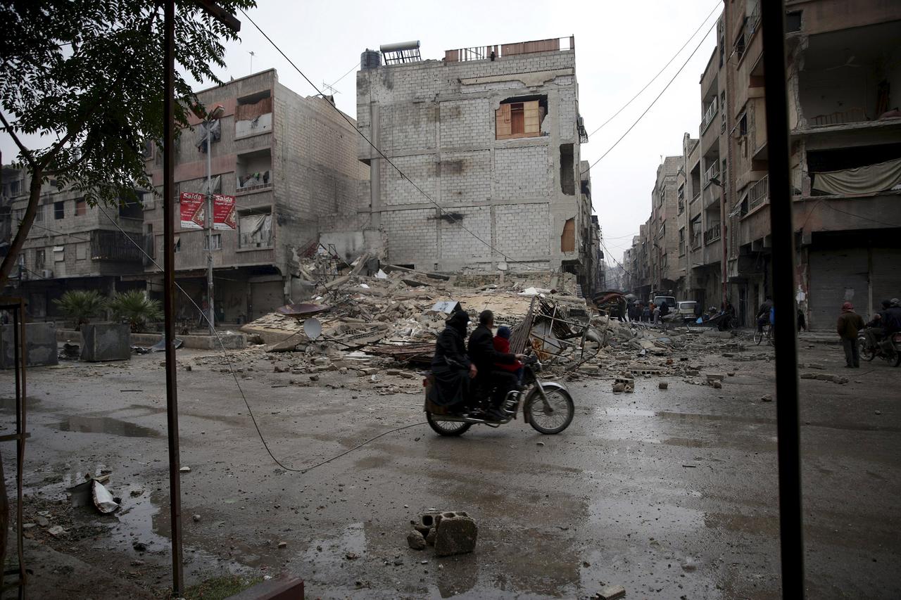 Residents ride a motorbike near rubble of damaged buildings in the town of Douma, eastern Ghouta in Damascus, Syria November 17, 2015. REUTERS/Bassam Khabieh
