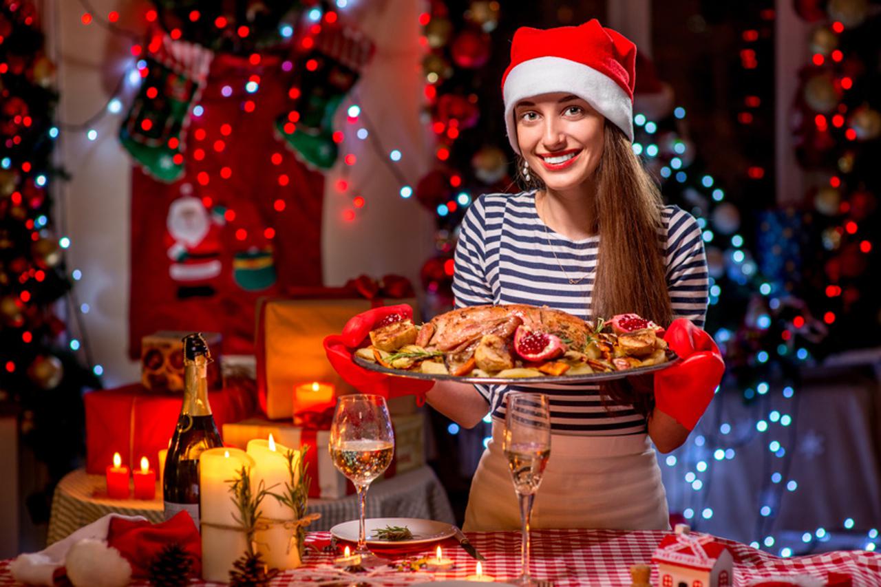 Woman with turkey garnished with potato and garnet dressed with Christmas hat on festive light background