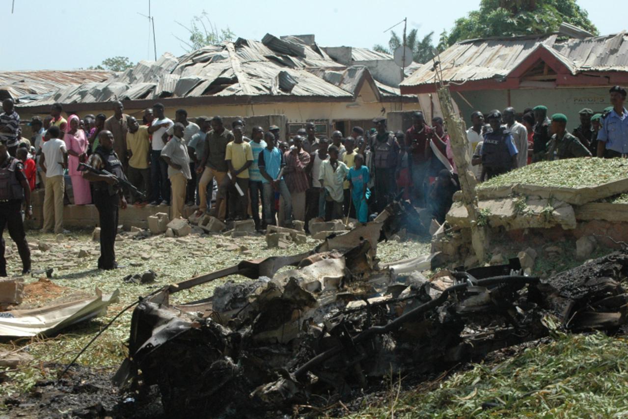 'Soldiers stand guard as people look at the remains of a burnt car after a suicide attacker drove a car bomb into a church in Kaduna, Nigeria, on October 28, 2012. The suicide bombing sparked fierce r
